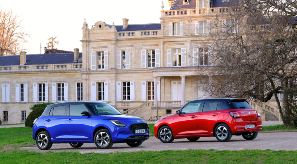 Blue and red Suzuki Swift hatchbacks parked in front of a historic European-style building, showcasing the model's stylish and compact design.